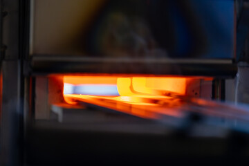 Zoom sur un forgeron chauffant une barre de fer pour la préparer à être façonnée, dans un atelier artisanal.