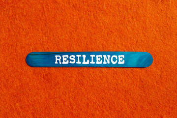 Resilience message written on blue wooden stick on orange background. Conceptual resilience symbol....