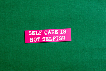 Self care is not selfish message written on pink paper sticker on green background. Conceptual self...