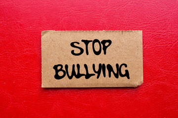 Stop bullying message written on ripped torn cardboard paper piece on red background. Conceptual...