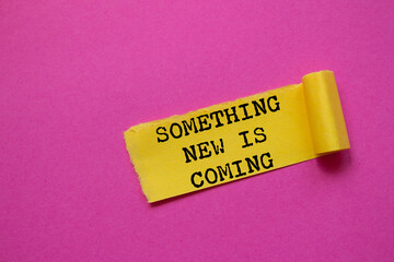 Something new is coming message written on ripped torn yellow paper piece on pink background....