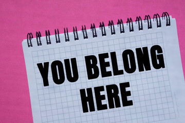 You belong here message written on notebook page on pink background. Conceptual you belong here...