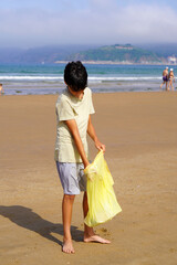 preteen boy picking up plastics on the beach sand