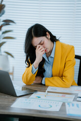 Asian businesswoman stressed holding crumpled paper while working with laptop and documents in...