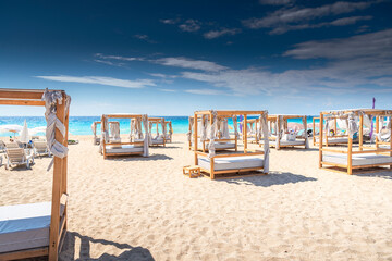 Luxurious empty canopy beds on a tropical beach with soft sand and turquoise sea under clear blue sky. Seaside resort vacation concept