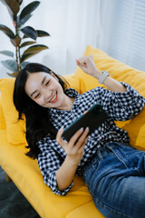 Young Asian woman at home playing using mobile phone and sending online messages to friends through...