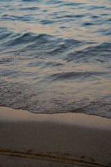 Gentle Sea Wave Touching Sandy Shore at Sunset. High quality photo. A peaceful close up of a gentle sea wave lapping against a sandy beach during sunset. The soft golden and pink hues of the sky are