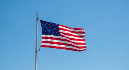 Fototapeta premium American Flag Waving in Blue Sky - A vibrant American flag billows in a clear blue sky, symbolizing freedom and patriotism
