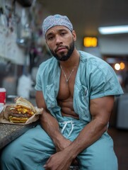 Man in medical scrubs with a cap sitting at a counter with a burger in a casual indoor setting