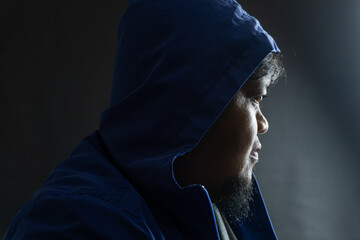 Indonesian man with beard and blue hooded nylon jacket, head covered and face partially hidden,...