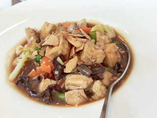 A savory Chinese-Indonesian dish, Sapo Tahu or claypot tofu, featuring soft tofu, vegetables, chicken, and mushrooms in a thick brown sauce, served on a white plate with a spoon.
