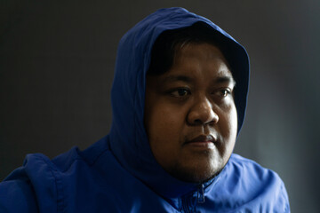 Indonesian man with beard and blue hooded nylon jacket, head covered and face partially hidden,...
