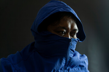 Indonesian man in his 30s with beard and blue nylon jacket, head and part of face obscured by hood,...