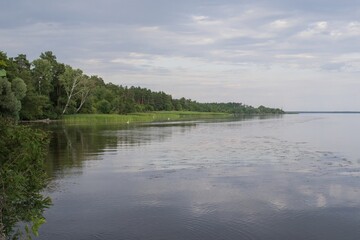 Calm river landscape with forest bank, blue sky and calm water in summer