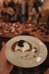 Female hand holding ceramic plate with sweet cream tartlet with berries