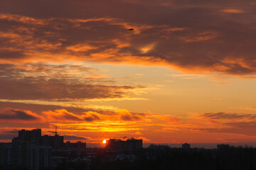 Dramatic fiery orange sunset sky with scattered clouds over city skyline. Warm golden light, silhouette of buildings, peaceful end of day in urban landscape