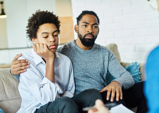 Father with his teenage son at meeting with social worker, psychologist discussing mental health family sitting on sofa in psychotherapist office