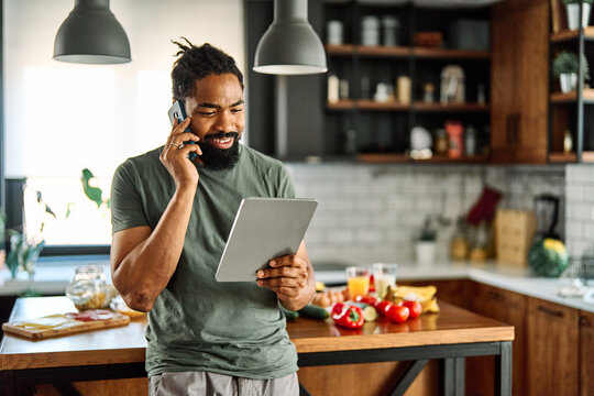 Happy young afro american man having fun preparing food and looking for recipes online using a tablet in kitchen, or a young businessman working from home office making connections online, talking mak