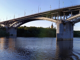 Fototapeta premium Majestic arched bridge over calm river at sunset, with Orthodox church dome in distant background