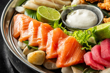 Close-up of fresh salmon and tuna sashimi with lime, lettuce, and sauce, artfully arranged on natural pebbles and leaves. High-end gourmet presentation, ideal for food themes.
