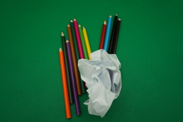 Colorful pencils scattered around a crumpled paper on a vibrant green surface during an artistic...