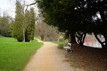 Serene pathway along the riverbank with a white bench inviting moments of reflection on a cloudy...