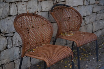 Worn wicker chairs resting against a rustic stone wall in a quiet garden reflecting the calm of a sunny afternoon