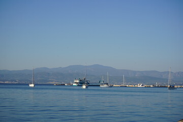 Sailboats gently gliding on calm waters at dawn near a tranquil harbor surrounded by distant mountains and clear skies