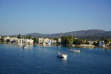 Sailboats glide peacefully on the tranquil waters of a picturesque harbor surrounded by charming seaside homes under a clear blue sky
