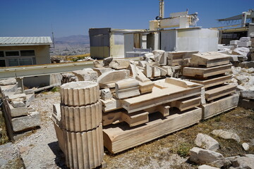 Remnants of ancient architecture atop a historical site under the bright midday sun, showcasing fragments of columns and stones awaiting restoration