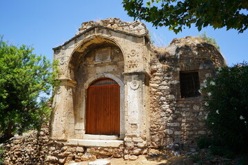 Historical stone structure with a grand wooden door surrounded by lush greenery under a vibrant blue sky in a tranquil location