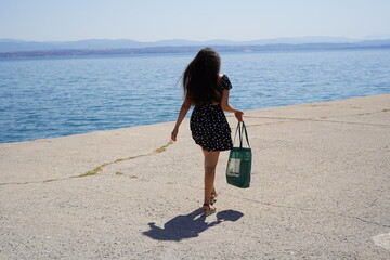 Joyful stroll by the tranquil water on a sunny day with a vibrant outfit and a stylish bag in hand, capturing carefree moments of summer bliss