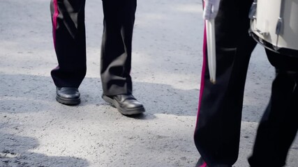 A lively group of uniformed percussionists marches in synchronization on a paved street, capturing the rhythmic energy and movement of a vibrant public performance.