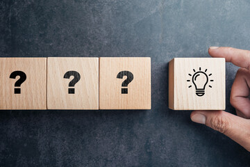 Hand holding a wooden block with a lightbulb next to blocks with question marks, concept of finding...