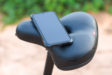 A smartphone resting on a black bicycle saddle outdoors. Concept of cycling, navigation, fitness...