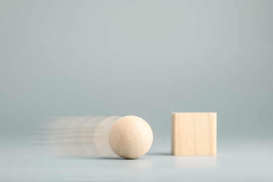 A moving wooden sphere quickly overtakes a stationary wooden cube. Concept of agility, speed, and flexibility outperforming rigidity and stagnation
