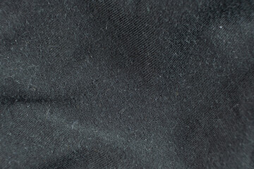 Macro texture of black fabric with lots of pilling and damage on the surface.