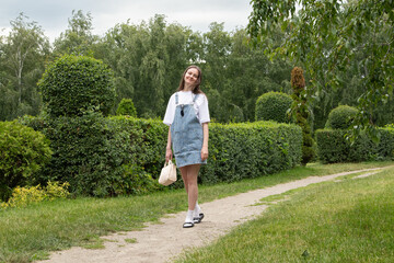 A young woman walks along a gravel path in a beautifully landscaped garden filled with green hedges...