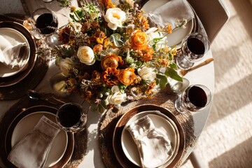 Top-down view of a Thanksgiving table set for four: plates, cutlery, wine glasses and fall floral centerpiece, warm light from window