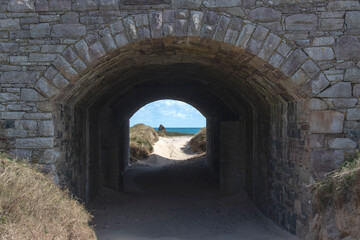 Alderney Channel Islands beach and view through stone arch to golden sandy beach called arch beach