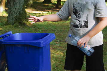 children clean up the forest by throwing empty bottles into a bag and a trash can