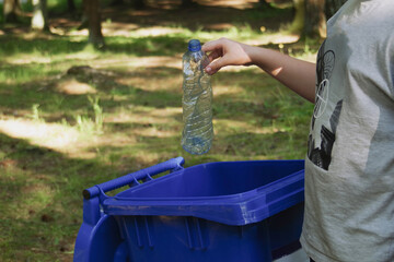 children clean up the forest by throwing empty bottles into a bag and a trash can