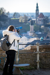 Mujer turista usando uno de los telescopios del castillo de Salzburgo para admirar las vistas de Austria. Fotografía vertical