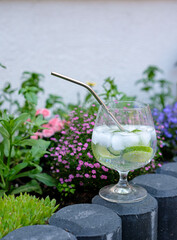 A gin and tonic glass is placed among flowers at home. Tranquil atmosphere of home relaxation.