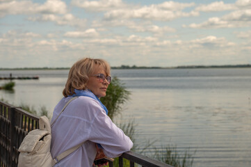 Fototapeta premium Mature adult woman on the lake bank looks far.