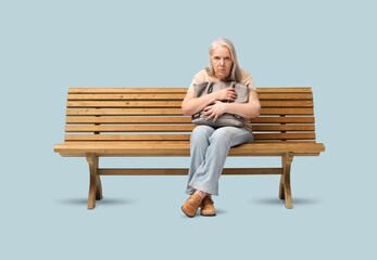 Scared mature woman sitting on a wooden bench, clutching her handbag tightly with a fearful...