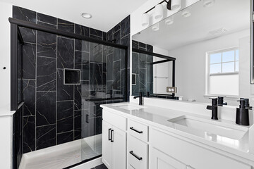 A bathroom with a white cabinet, black faucets on a quartz countertop, and black tiled shower.
