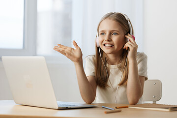 Young girl with headphones smiling while talking via laptop, showcasing remote learning and interactive communication in a bright setting