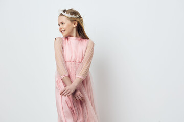 Charming young girl in a pink dress with long sleeves, smiling joyfully against a light background,...