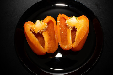 Orange bell pepper, half and slices isolated on black plate. Concept food preparation process.